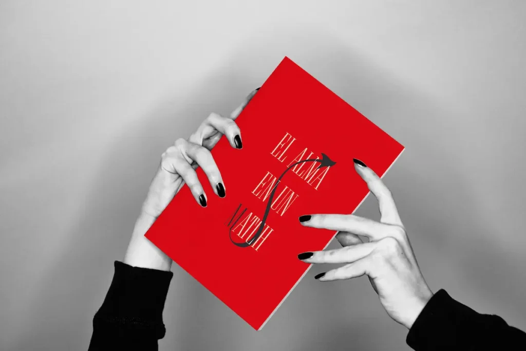 Manos sosteniendo un libro rojo con el texto "El alma en un madri" en diseño gráfico editorial.