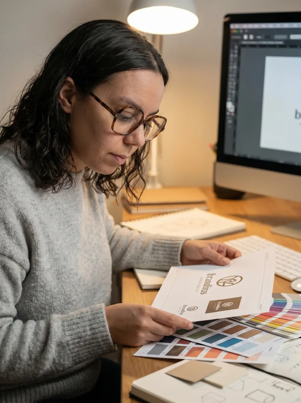 Mujer revisando documentos de branding junto a una paleta de colores en su escritorio de diseño.
