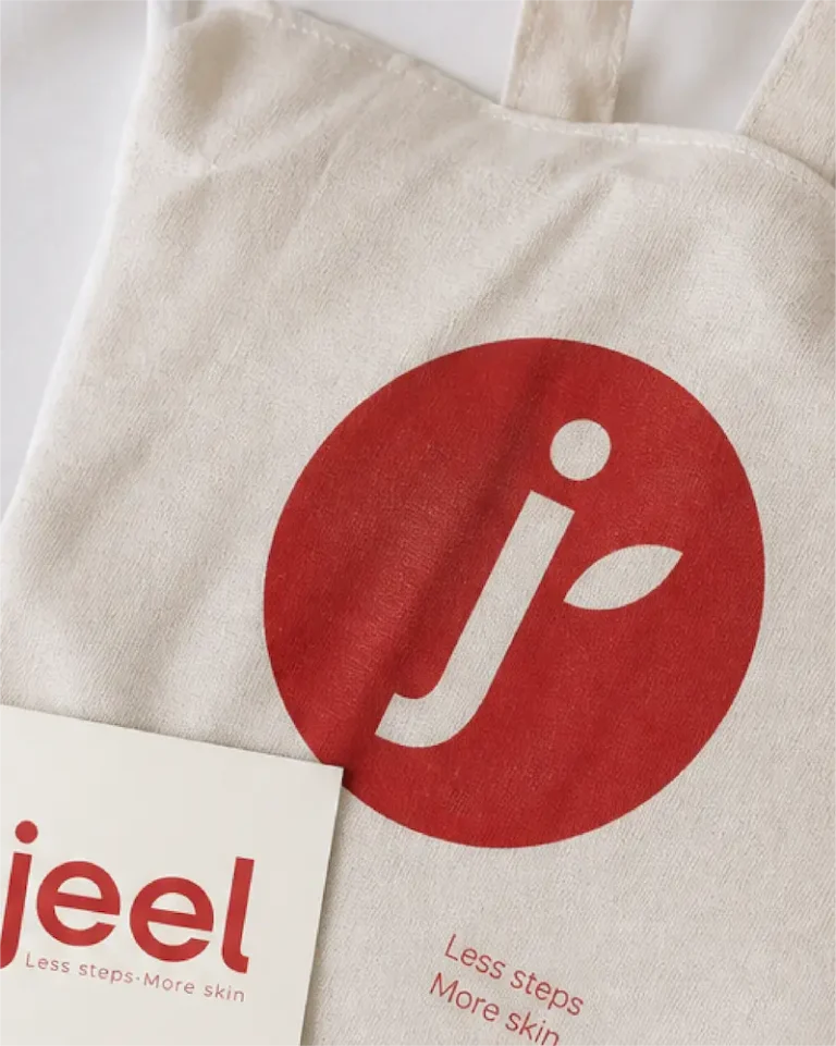 Tote bag de Jeel con el isotipo en un círculo rojo y tarjeta con el logotipo
